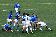 Photographie d'un regroupement dans un match de rugby à XV, entre l'équipe d'Italie en maillots bleus et l'équipe de France en maillots blancs