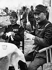 Schwarzweiss-Foto von zwei japanischen Soldaten, die an einem Tisch sitzen.