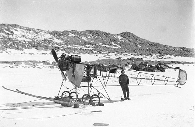 Photo en noir et blanc d'un avion sans ailes sur la neige, un homme s'appuyant sur sa queue.