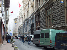 A city street, with several parked vans, flanked by stone buildings alongside