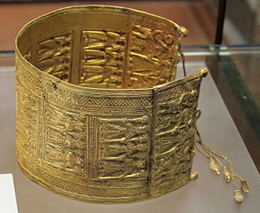 Vecchio braccialetto d'oro, inciso con piccole figure e raffinati ornamenti.