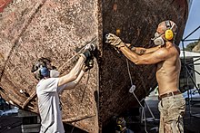 Two people sanding the hull of a ship to remove rust Des benevoles poncent la coque du Kraken a Savone ete 2020.jpg