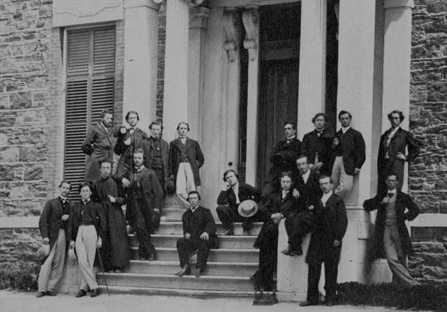 A group of men assembled on the front steps of a building, posed in formal wear