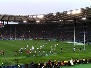 Match de rugby opposant des joueurs en maillots bleus et d'autres en maillots blancs.