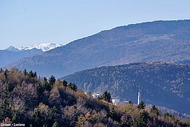 Il campanile di Lusiana fotografato dalla frazione di Tortima. Sullo sfondo i monti Forni Alti e Priaforà e, innevata, Cima Palon. In secondo piano il crinale del monte Corno