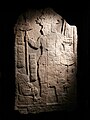 Estela maya fechada entre 300-900 AD. Fue tomada de una de las plazas en Aguateca. La imagen conmemora una victoria del gobernante de la ciudad: El dios Jaguar se representa en el escudo del guerrero y dos presos tienen los pies atados.