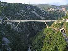 Vorgespannte starre Strebenrahmenbrücke, die eine Straße über eine steile Flussschlucht zwischen zwei Tunneln trägt