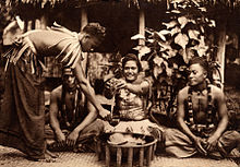 Kava ('ava) makers (aumaga) of Samoa. A woman seated between two men with the round tanoa (or laulau) wooden bowl in front. Standing is a third man, distributor of the 'ava, holding the coconut shell cup (tauau) used for distributing the beverage. Samoan 'ava ceremony, c. 1900-1930 unknown photographer.jpg