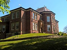 Ein großes rotes Backsteinhaus auf einem grasbewachsenen Hügel