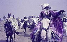 Rich horsemen at the Sallah festivities in Bauchi, 1970-1973. ASC Leiden - Rietveld Collection - Nigeria 1970 - 1973 - 01 - 056 Sallah festivities in Bauchi. Rich horsemen in white and pink. Rider with a trumpet.jpg