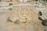 Photograph of a large, weathered, stone capital resting on the ground, with a low-relief cross enclosed in a cartouche