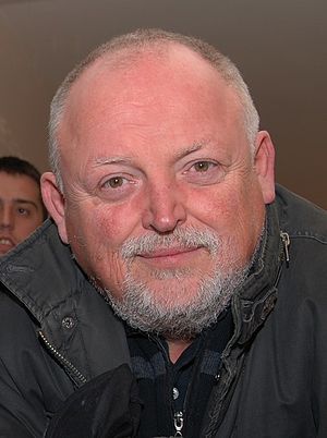 Middle-aged Caucasian male with short hear and facial hair, wearing black jacket and smiling at camera