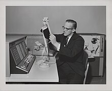 User holding paper tape at the IBM 1620 with the IBM 1621 paper tape reader in background, IBM headquarters, White Plains, NY, 1961 IMB1620 and IBM 1621 with paper tape.jpg