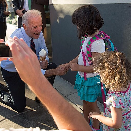 Joe Biden holding an ice cream cone, kneeling and shaking hands with a little girl