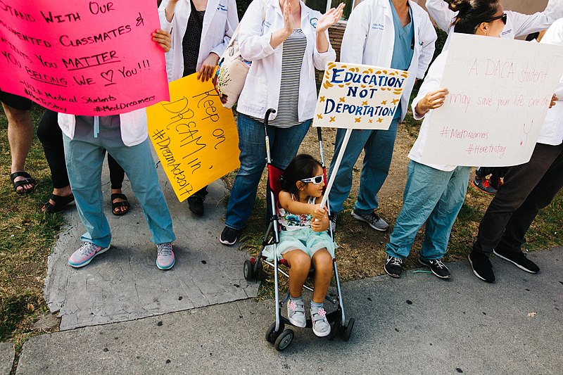 a child in a stroller holds a sign at a protest reading "Education Not Deportation"