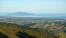 A view from multiple kilometers back from the coastline. Areas of urban development are visible with Kapiti Island in the background