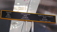 Uma placa multilíngue no Terminal Marítimo de Passageiros do Porto Exterior em Macau; em cima está em português e chinês, que são as línguas oficiais de Macau, enquanto em baixo japonês e inglês, que são línguas comuns usadas pelos turistas da cidade