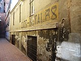 *2012-Ortigosa 10-12 interior. En primer terme veiem una vella edificació de dues plantes, industrial, amb un rètol desfigurat que ens diu "SALDOS-RETALES", possiblement un magatzem de teixits.**Al fons de la fotografia i veiem un vell edifici amb les típiques reixes que s'instal·laven als centres de seguretat. Recordem que fins els anys 37 ò 38 hi va haver un Centrre de Seguretat o, Caserne de Policia, "Delegación de Vigilancia".