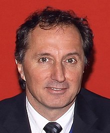 Portrait of Peter Bogner wearing a business suit in front of a red carpet background