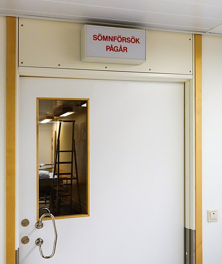 Sign with text: Sömnförsök pågår (Sleep study in progress), room for sleep studies in NÄL hospital, Sweden.