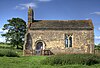 Une petite église en forme de chapelle vue du sud, avec un clocher à gauche, une porte et une fenêtre unique