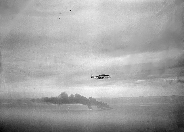 A U.S. Navy TBM Avenger flies past three Japanese oilers burning in Cam Ranh Bay, 1945