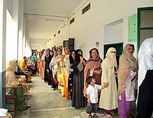 Photo en couleur montrant des femmes majoritairement voilées faisant la queue dans un couloir