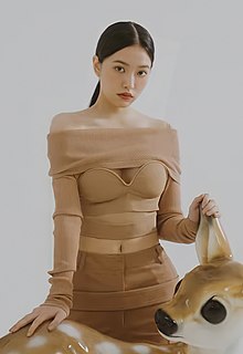 Yeri standing, looking at the camera, and placing her hands on a deer sculpture