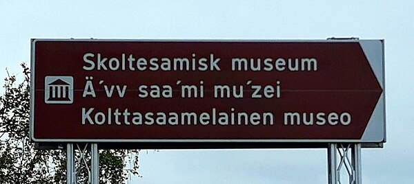 Road sign for the Äʹvv Skolt Sámi Museum [no] in Neiden, Norway. Starting at the top, the lines are in Norwegian, Skolt Sámi, and Finnish.