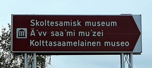 Road sign for the Äʹvv Skolt Sámi Museum [no] in Neiden, Norway. Starting at the top, the lines are in Norwegian, Skolt Sámi, and Finnish.