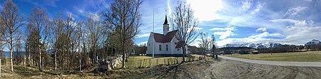 Bjarkøy kirke ble opprinnelig reist i 1766 på Sandsøya, men ble flyttet og gjenreist på Bjarkøya i 1886. De snøkledte fjellene bak ligger på Grytøya. Fortegnet panorama: 2019