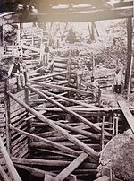 Fotografia em preto e branco mostrando um grupo de trabalhadores em frente a uma grande vala fortemente escorada.