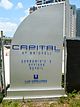 A large, curved, silver sign that reads "Capital at Brickell Condominiums Offices Retail"; a sandy construction site is in the background
