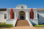 The design bears little resemblance to the local architecture of the time. The small elliptical gable on short pilasters is dated 1804. There is a straight gable at the back, obviously mid-19th century. The Drostdy has a large hall. The full depth of the Construction began in 1804 on the farm Rietvlei that had belonged to a Hercules du Pre. The ex-landdrost, Bletterman of Stellenbosch, originally drew up plans for the Drostdy, but after some progress had been made, by order of landdrost Van de Graaff the design was changed to a plan by Louis- Michel Thibault. Much to the concern of Governor Janssens, the building took longer and cost more to be completed than had been anticipated, being finally finished in 1807. It is one of the few extant buildings at the Cape of which Thibault is the undisputed architect. The Drostdy had already fallen into a state of disrepair by 1822, a reason put forward for making Worcester the seat of the drostdy instead of Tulbagh. The Drostdy was sold to a young settler named Heatlie, after which it remained a private dwelling with a small farm. Towards the end of the century it again fell into disrepair, but was restored by Sir Meiring and Lady Beck. It burnt down in the mid-1930s, and was again restored. The 1969 Tulbagh earthquake caused further extensive damage. It was then acquired by the National Monuments Council and, during 1973, restored for the third time. The building is now in use as offices, reception rooms and museum The outbuildings flanking the dwelling have been demolished; the one on the right since having been rebuilt. Type of site: Drostdy. Drostdy 01.jpg