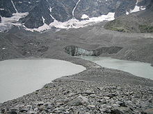 Au premier plan la moraine médiane séparant en deux le lac du glacier d'Arsine visible au second plan avec sa falaise de glace au centre de l'image, au dernier plan se trouve le pied des falaises constituant le cirque.