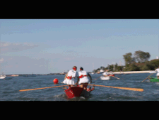 Mujeres que reman en barco rojo, en la laguna de Venecia. Día soleado. Mujeres vestidas con una camiseta blanca y una minifalda blanca.