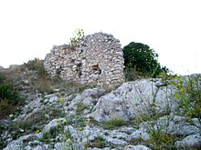 Un bout de mur en petites pierres, ruiné, construit au-dessus d'un bloc rocheux