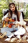 Un hippie con una tunica variopinta e i capelli lunghi sta suonando la chitarra