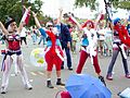 Women dressed in red, white, and blue outfits with missiles strapped around their hips do cheers in the street.