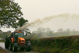 Drijfmest wordt vanop de weg over een haag het veld op gespoten