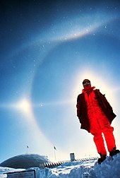 Halo display at the South Pole (1980), featuring a parhelion, 22deg halo, parhelic circle, upper tangent arc and Parry arc. Diamond dust is visible as point-like reflections of individual crystals close to the camera. Sun halo optical phenomenon edit.jpg