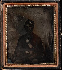 Three quarter portrait, young soldier seated, in Union uniform with kepi; tents (possibly painted backdrop) in background. Cased tintype, sixth plate.jpg