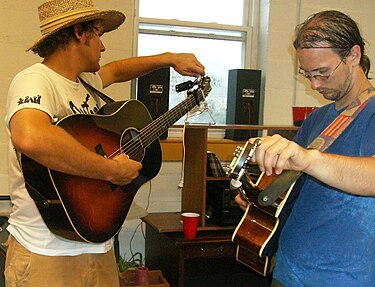 Acoustic guitars being tuned up backstage before a concert; note the tiny electronic tuner clipped to the headstock of the guitar on the left. Trent Wagler and Chris Howdyshell tuning guitars Lawn Jam Our Community Place Harrisonburg VA June 2008.jpg