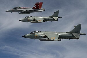 Two similar grey jet aircraft with high-mounted wing flying in formation with another red-tail fighter, which is leading and is furthest from photo. The leading jet is carrying an external fuel tank under fuselage.
