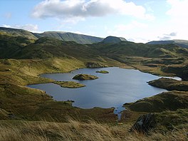 A small lake with two rocky islets surrounded by fells.