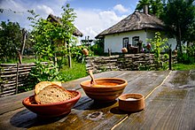 Eine Mahlzeit mit Borschtsch und Brot auf einem Holztisch, der im Hof ​​einer traditionellen Bauernhütte steht