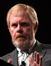 A picture of a red haired man with a beard and a mustache with a gray suit.