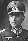 A man wearing a peaked cap and military uniform with an Iron Cross displayed at the front of his uniform collar.