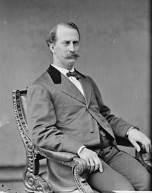 Black and white photo of Edward Miner Gallaudet seated in an arm chair. He has a handle-bar moustache and is dressed in a suit.