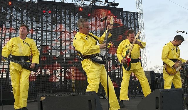 Devo performing live at the Forecastle Festival, in Louisville, Kentucky, 2010 Left to right: Gerald Casale (vocals; bass), Mark Mothersbaugh (vocals;